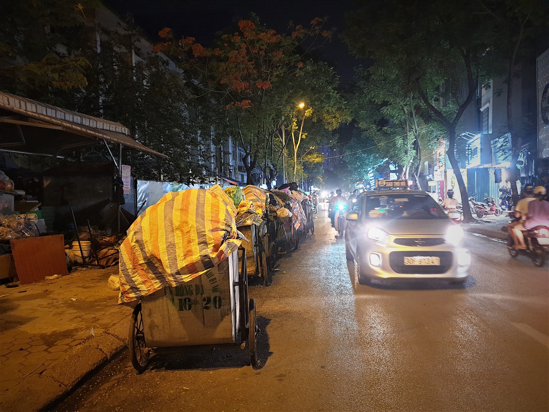 Tại nút giao Kim Mã - Đê La Thành, phố Chùa Láng, hàng dài xe gom rác vẫn phủ bạt chờ cẩu đến điểm tập kết.