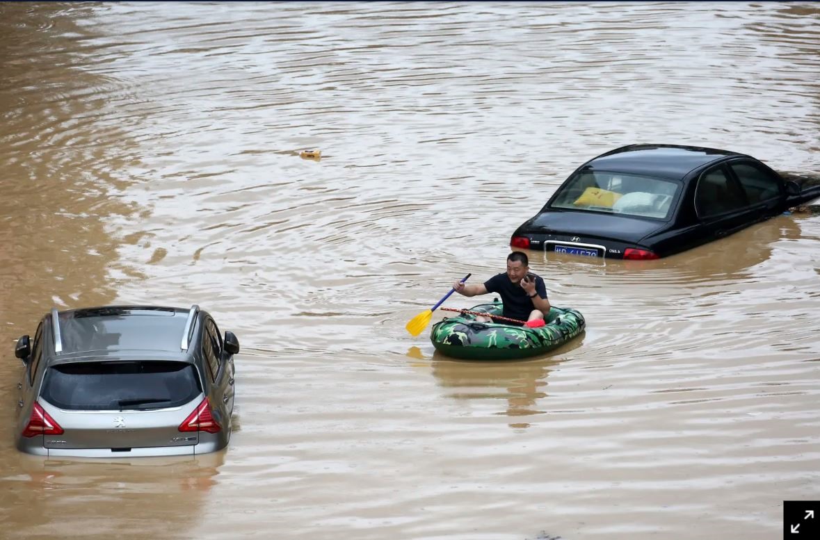 Một người đàn ông chèo xuồng đi qua những chiếc xe ô tô bị ngập trong nước lũ ở Quảng Tây, Trung Quốc. Ảnh: Tân Hoa Xã.