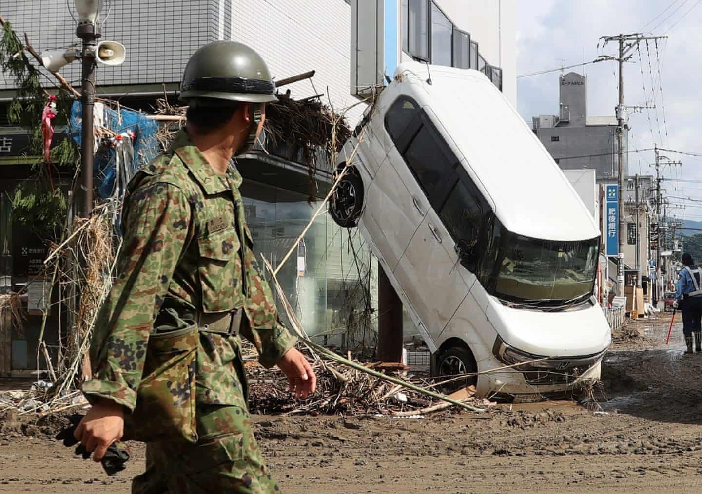 Một sĩ quan đi ngang qua một chiếc xe bị hư hỏng ở Hitoyoshi, thuộc quận Kumamoto Ảnh: AFP.
