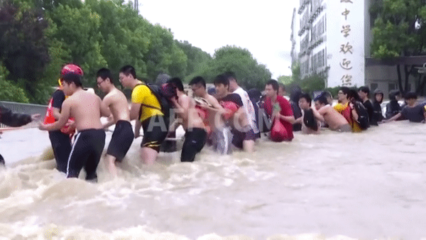Lội bì bõm qua dòng nước lũ để tới điểm thi. Ảnh: AFP