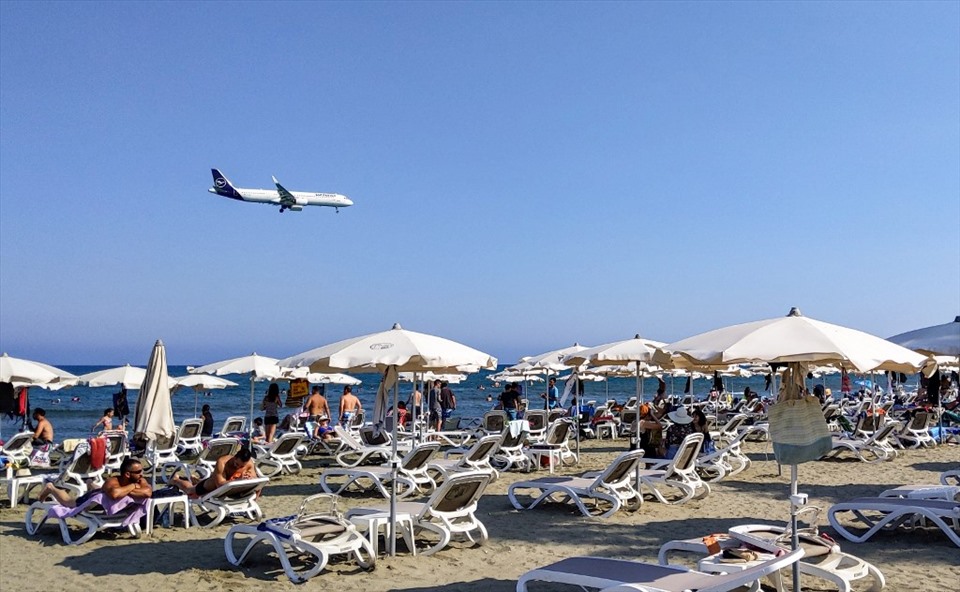 Ảnh chụp ngày 1.8.2020 cho thấy một máy bay chở khách đang hạ độ cao hướng tới sân bay quốc tế Larnaca trên đảo Cyprus đang bay phía trên bãi biển Địa Trung Hải đầy ắp du khách. Ảnh: AFP.