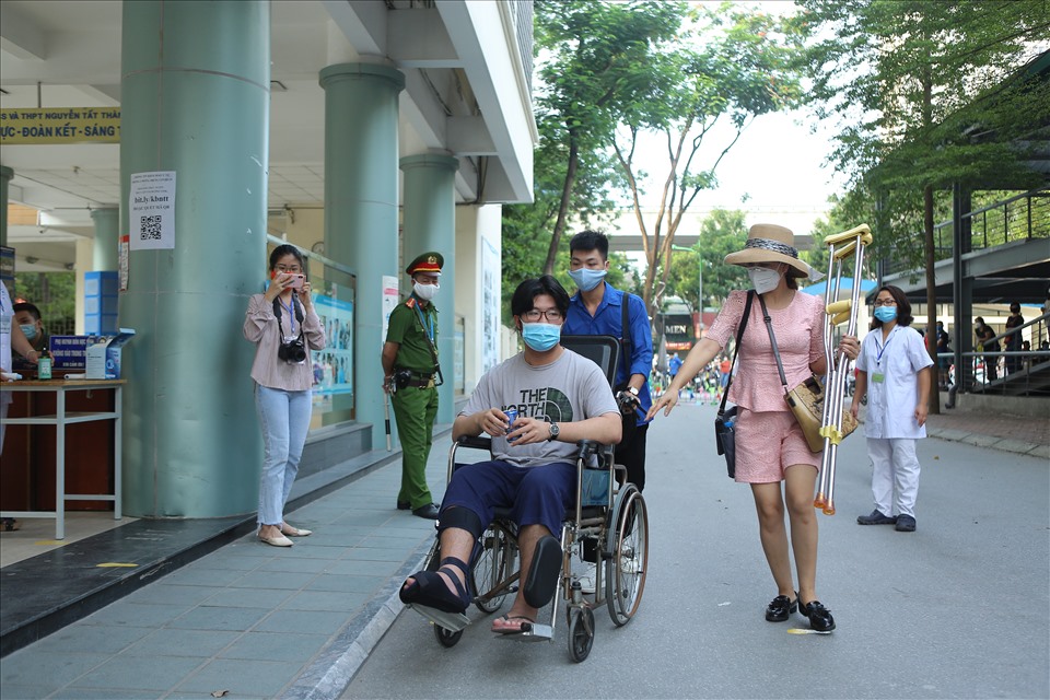 Tại điểm thi THPT Nguyễn Tất Thành, một em học sinh phải ngồi xe lăn tới dự thi và nhận được sự giúp đỡ nhiệt tình của các tình nguyện viên. Ảnh: Danh Nhân.