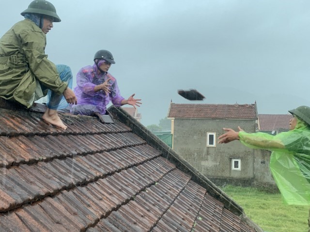 Mặc cho mưa lớn, cán bộ, chiến sỹ Công an Nghi Xuân cùng các lực lượng khác đang khẩn trương lợp lại nhà dân bị tốc mái. Ảnh: NX.