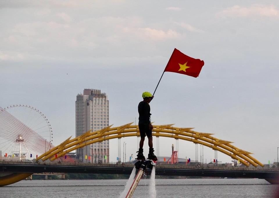 Lá cờ Tổ quốc tung bay trên tay người vận động viên lướt ván trên sông Hàn. Ảnh: Đặng Thu Thủy