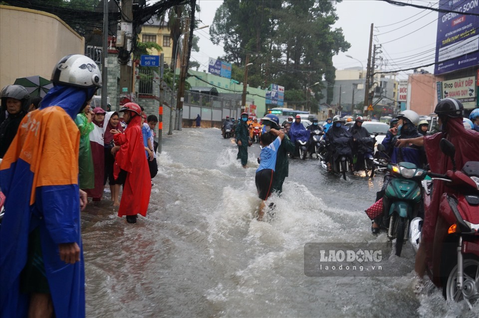 Nước chảy cuồn cuồn trên đường Võ Văn Ngân cũng khiến các em học sinh tam học vất vả về nhà. Trong ảnh, một em học sinh được dân phòng quận Thủ Đức hỗ trợ qua đường. Ảnh: Minh Quân