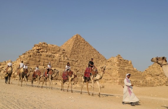 Hướng dẫn viên du lịch dẫn du khách cưỡi lạc đà tham quan kim tự tháp Giza ở Giza, Ai Cập, ngày 21.10. Ảnh: Tân Hoa Xã