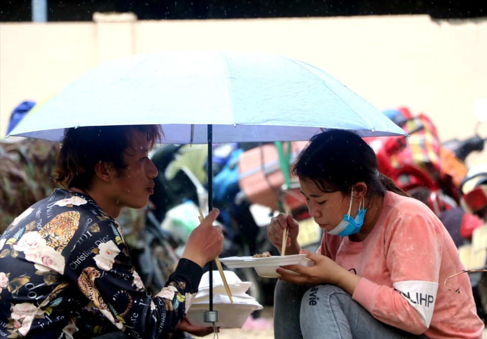 Đang ăn trời chợt đổ cơn mưa, đôi bạn trẻ chở che chiếc ô hoàn thành bữa cơm vội.