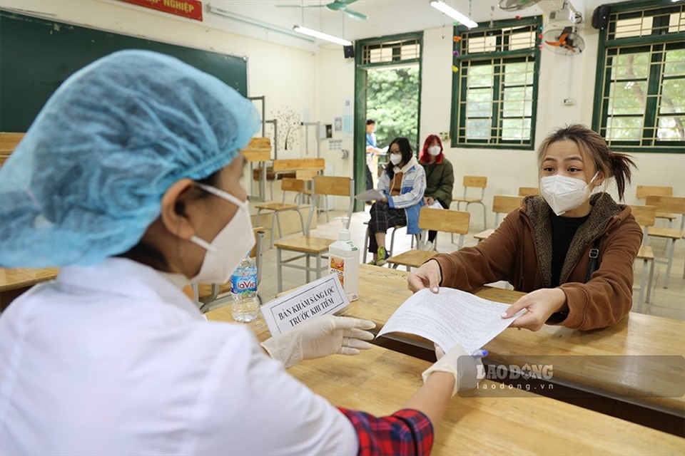 Học sinh trường THPT Trần Hưng Đạo đưa tờ khai tiêm chủng tới cán bộ Y tế để khám sàng lọc.