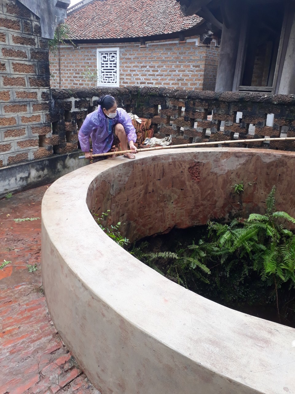 Người dân tham gia giám sát việc cọ rửa thành giếng làng, vớt những cọng rác rơi dưới giếng.