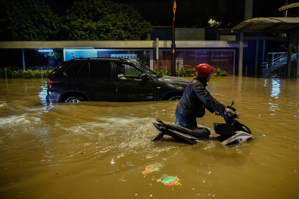 Một người dắt xe máy băng qua con đường ngập nước sau trận mưa lớn ở Kuala Lumpur. Ảnh: DPA
