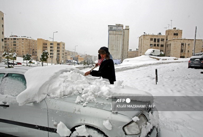 1. Một người đàn ông xúc tuyết phủ kín ô tô của mình sau trận bão tuyết ở thủ đô Amman của Jordan, vào ngày 18 tháng 2 năm 2021.