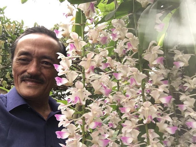 Nam nghệ sĩ mát tay Giang Còi bên những cành hoa lan trong vườn.