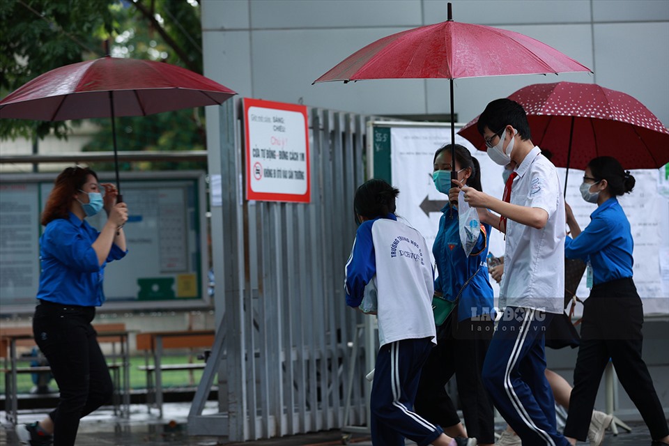 Tình nguyện viên che ô, đón các em học sinh vào điểm thi. Ảnh: Hải Nguyễn