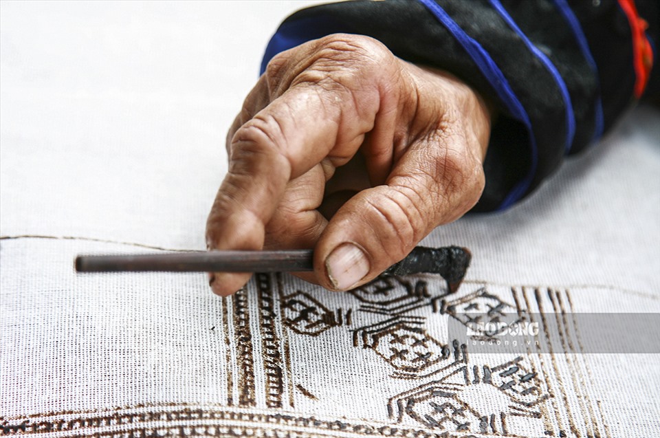 Người phụ nữ Mông dùng bút - một loại bút đặc biệt làm từ sừng hoặc xương của động vật, sau đó chấm sáp ong đang nóng chảy để vẽ hoa văn trên vải lanh.