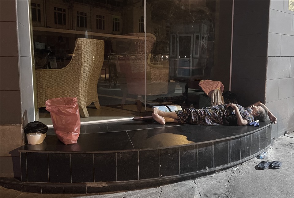 Bà T.V nằm ngủ tại bậc cửa ra vào của một quán cà phê trên đường Lê Duẩn. Trước đây, bà bán trà đá phía đối diện cổng ga Hà Nội. Từ ngày thành phố giãn cách xã hội, bà chuyển sang đi bới rác, nhặt ve chai.
