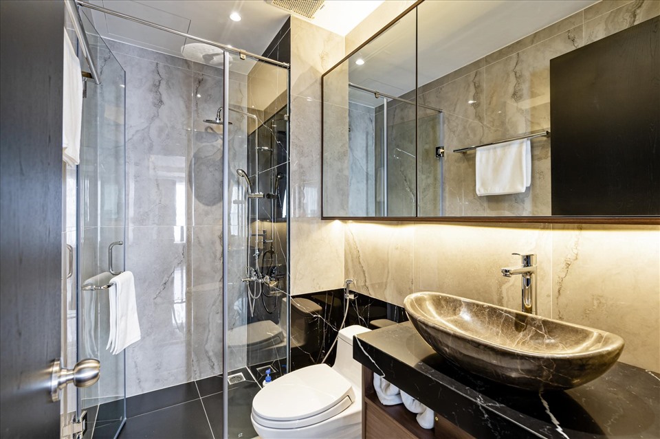 Một trong hai nhà vệ sinh của căn hộ. Phòng được ốp đá vân tone đen xám vô cùng sang trọng và sạch sẽ. Tủ kệ gắn tường kết hợp với gương giúp tối đa diện tích.