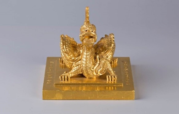 Ấn đúc bằng chất liệu vàng 10 tuổi, tạo thành 2 cấp hình vuông, quai là tượng rồng uốn khúc, đầu vươn về phía trước, hai sừng dài, đuôi xòe 9 dải hình ngọn lửa, chân rồng 5 móng.