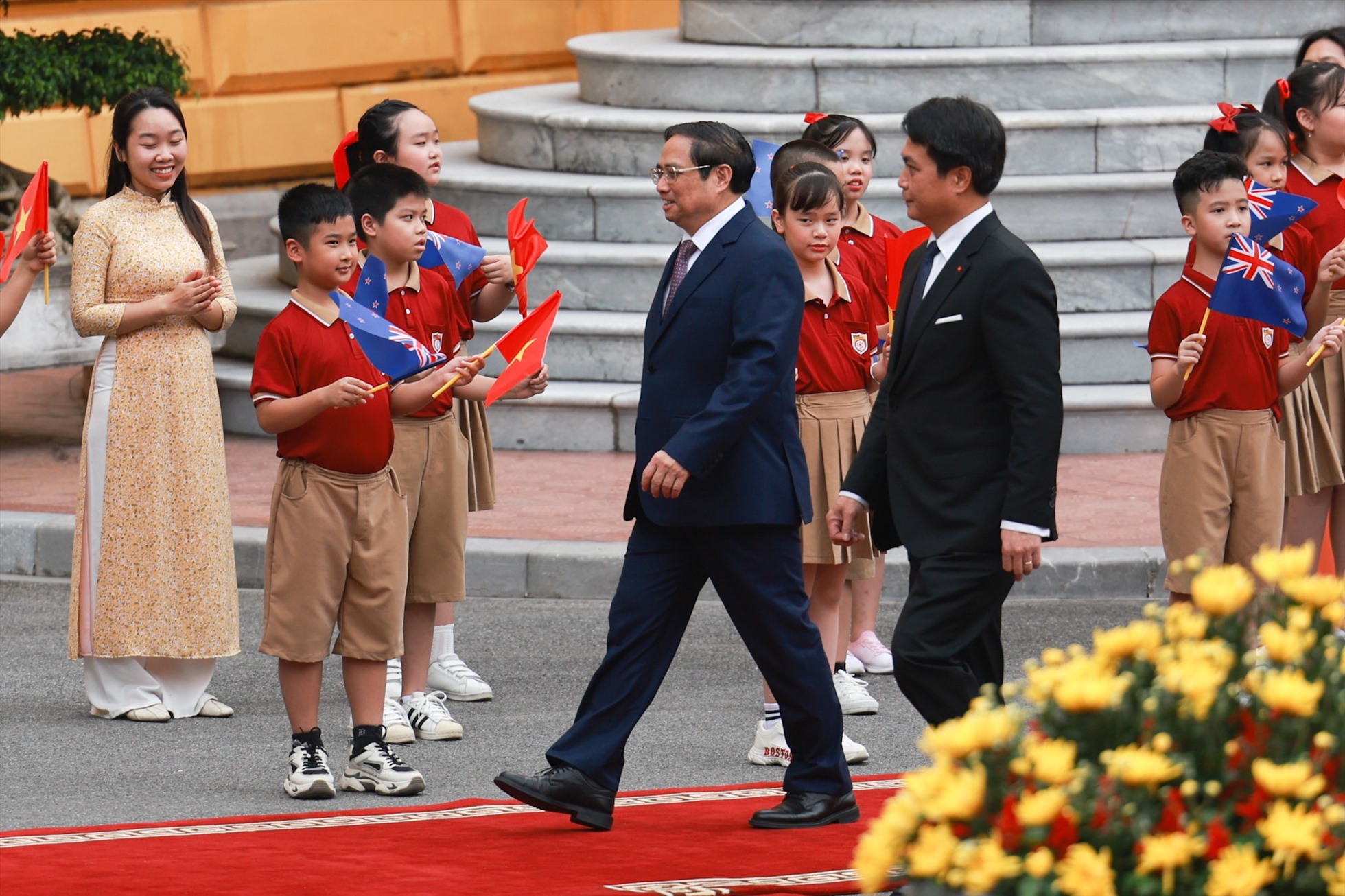 Thủ tướng Phạm Minh Chính đón Thủ tướng Jacinda Ardern trong tiếng vẫy chào của các em học sinh với cờ hoa rực rỡ trên tay. Ảnh: Hải Nguyễn