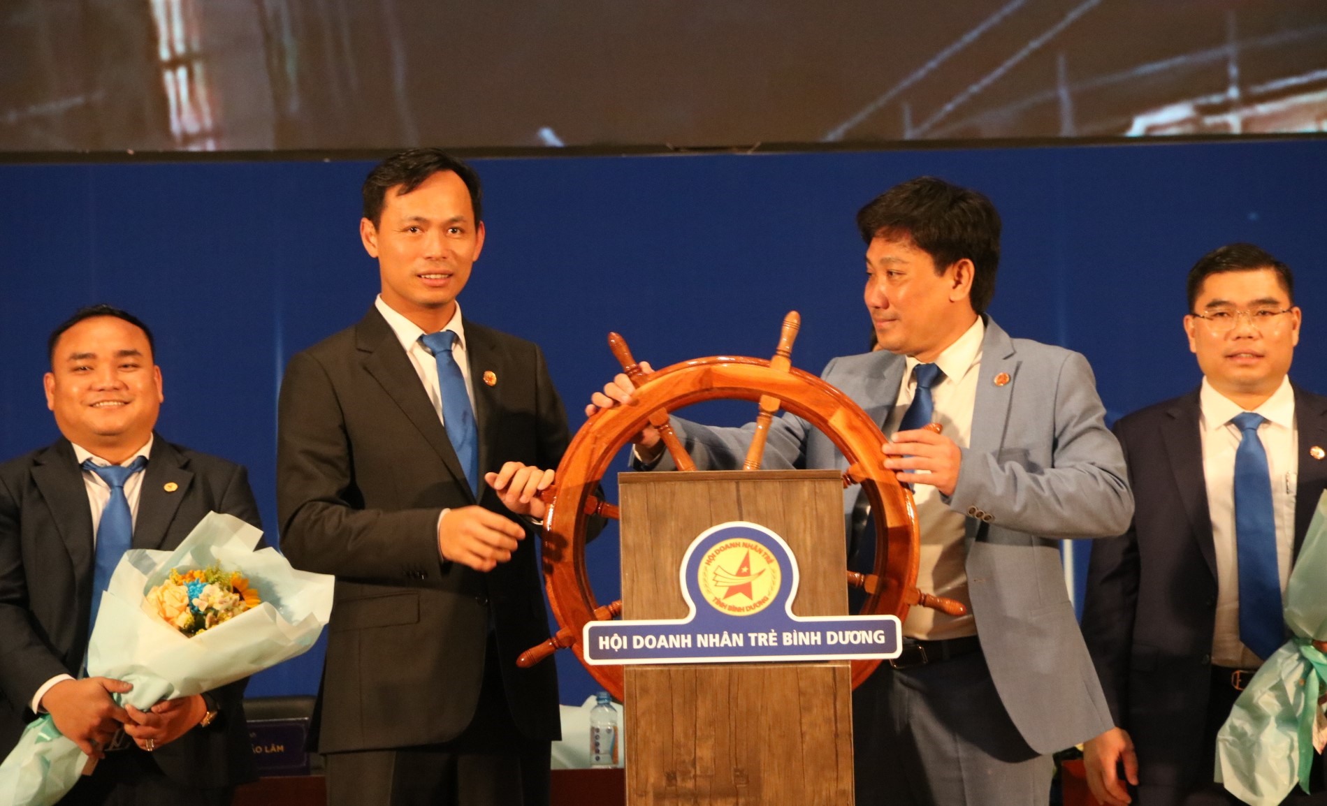 Ông Võ Sơn Điền (bìa phải) và ông Huỳnh Trần Phi Long (bìa trái) trên biểu tượng bánh lái con thuyền Hội Doanh nhân trẻ Bình Dương. Ảnh: Đình Trọng