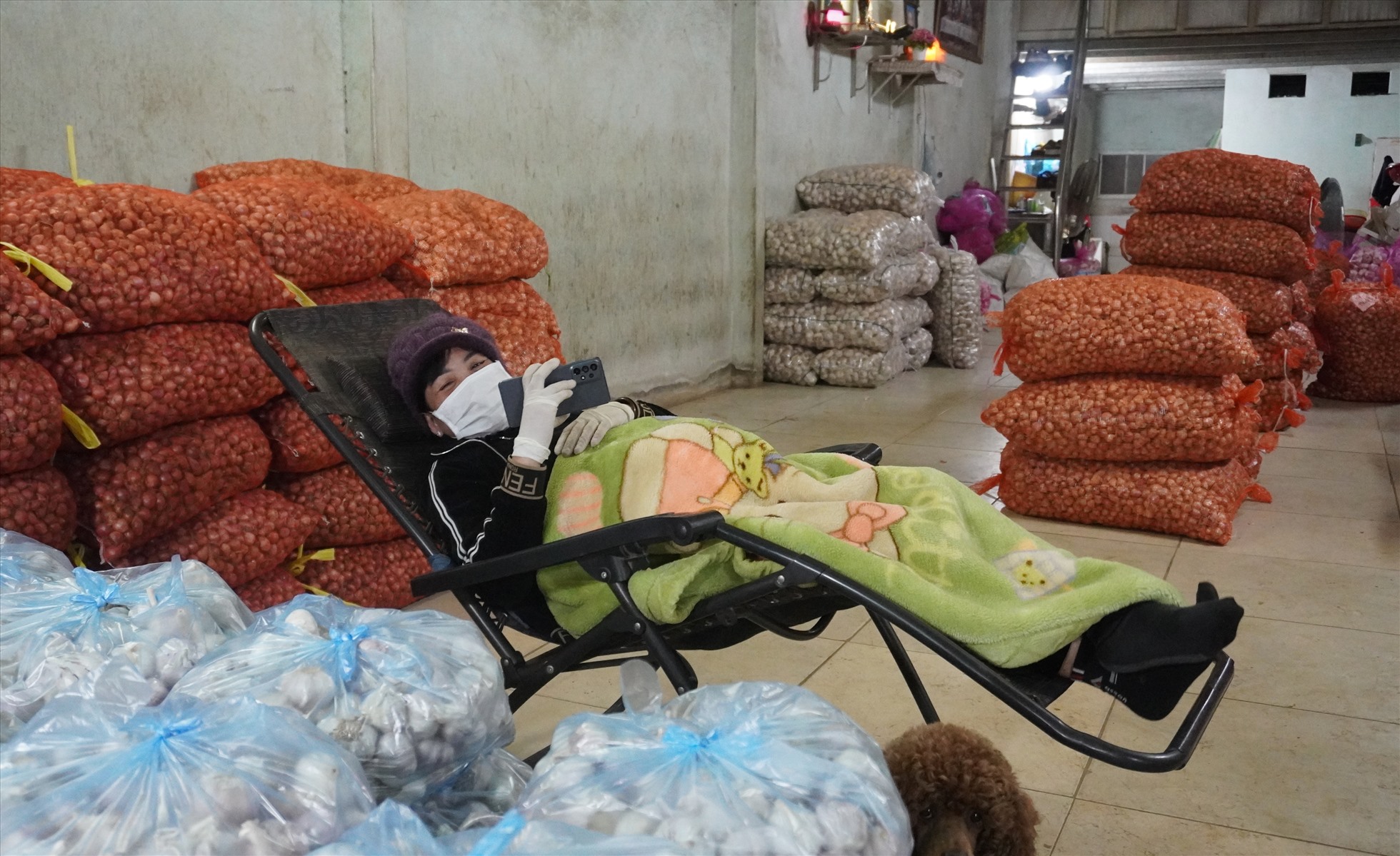 Các tiểu thương buôn bán tại chợ đầu mối Đông Hương co ro trong giá rét, dùng chăn quấn quanh người, ngồi chờ khách đến mua hàng. Ảnh: Quách Du