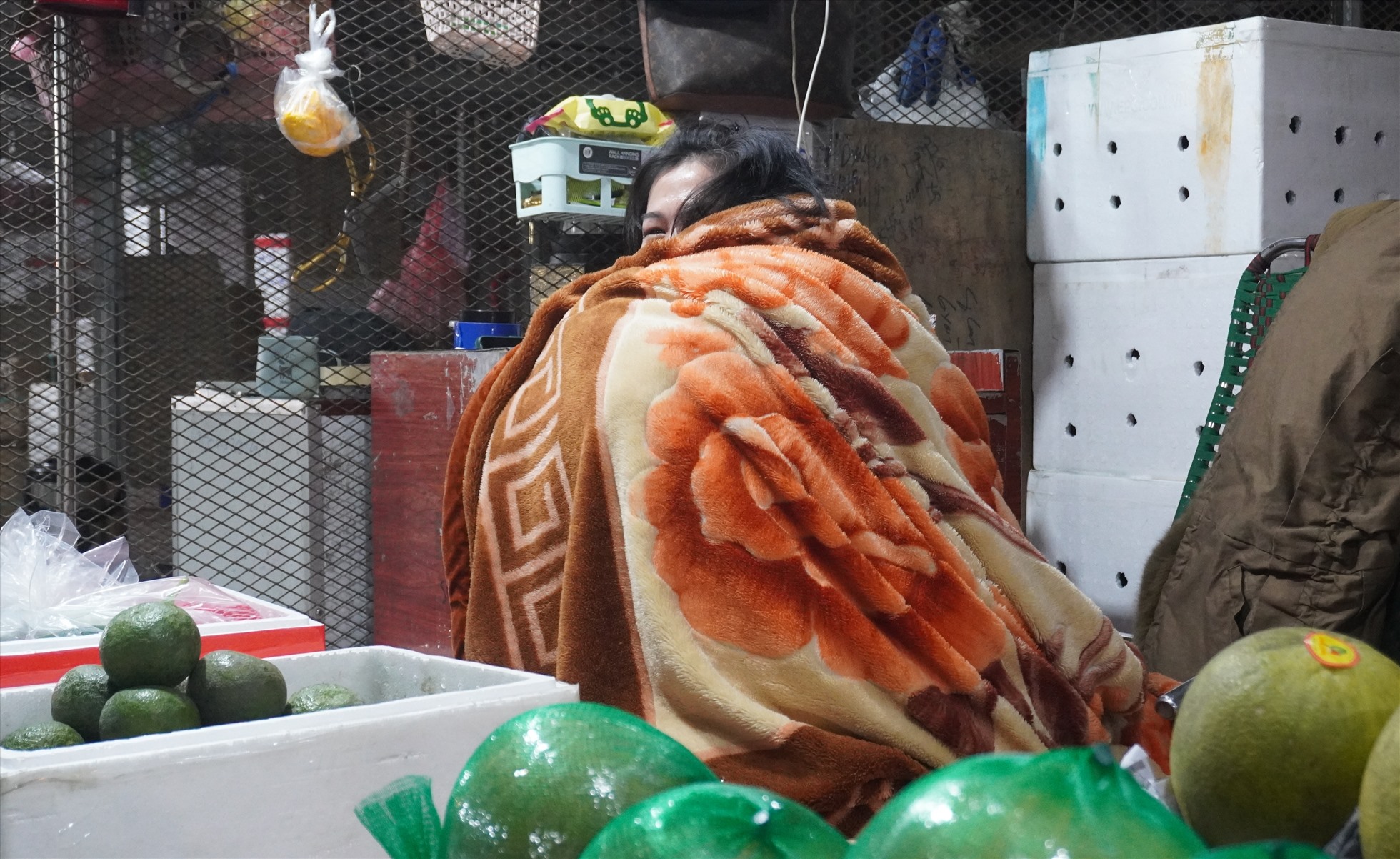 Các tiểu thương buôn bán tại chợ đầu mối Đông Hương co ro trong giá rét, dùng chăn quấn quanh người, ngồi chờ khách đến mua hàng. Ảnh: Quách Du