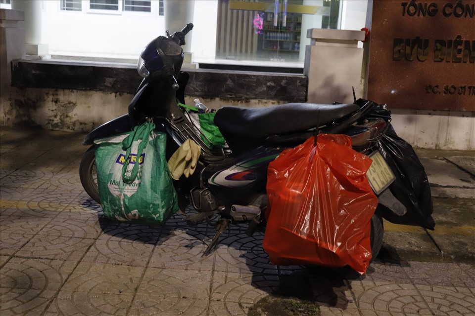 Chiếc xe máy mang theo đồ nghề, nước uống của công nhân vệ sinh môi trường quét dọn đường phố buổi tối. Ảnh: H.L