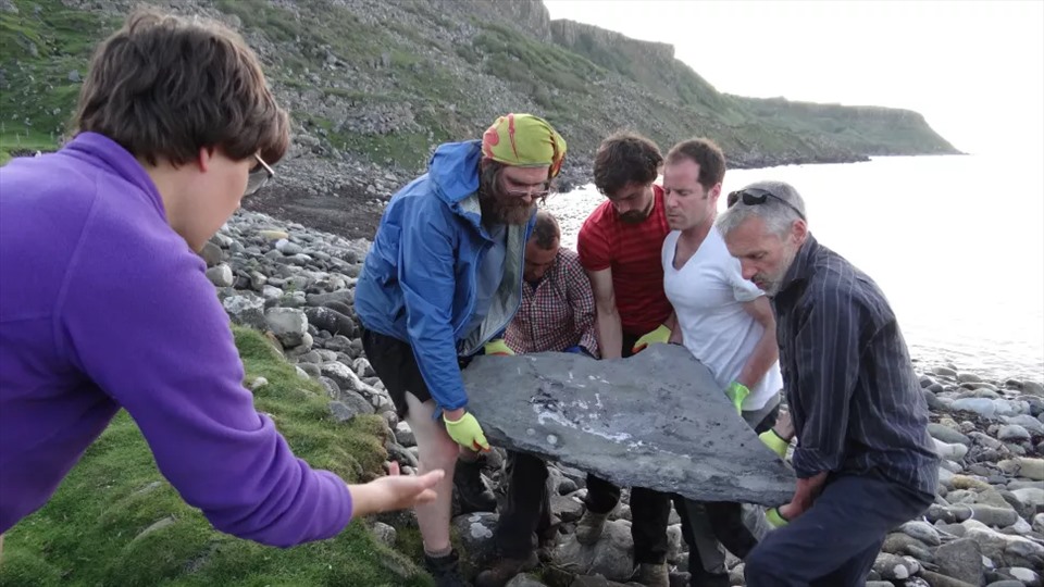 Scientists with the stone slab containing the fossil.  Photo: Scots Archeology