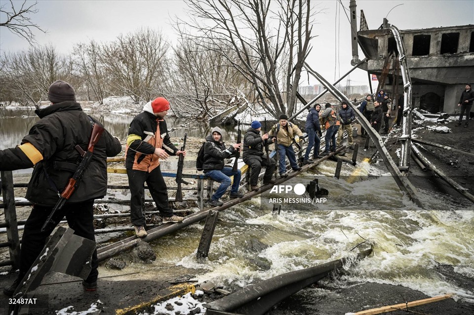Các thành viên của một đơn vị phòng thủ dân sự Ukraina chuyền súng trường tấn công mới sang phía đối diện cây cầu bị nổ ở mặt trận phía bắc Kiev vào ngày 1.3.2022. Ảnh: AFP
