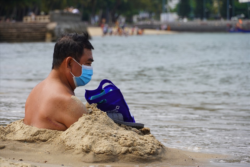 Một người đàn ông chôn mình dưới lớp cát sát mép nước. Ông Châu (quê Bạc Liêu) cho biết mình bị xương khớp nên ngâm mình trong nước cát và nước biển thế này sẽ có lợi cho việc điều trị. Ảnh: T.A