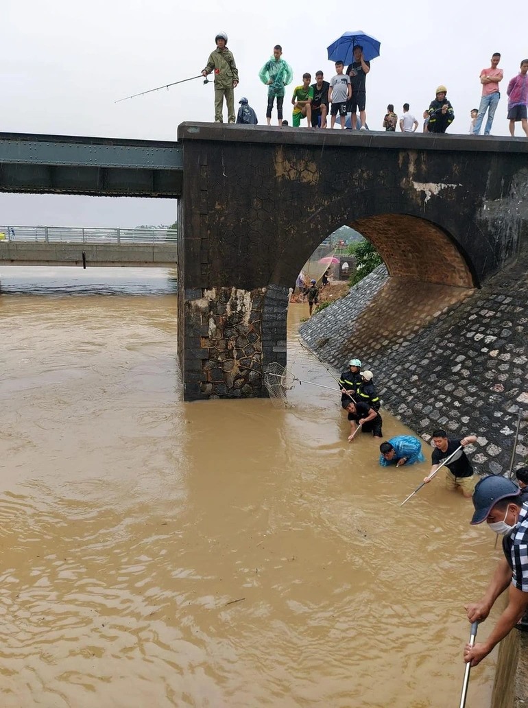 Hàng chục người dân dùng cần, vó, vợt bắt cá trên một khúc sông.