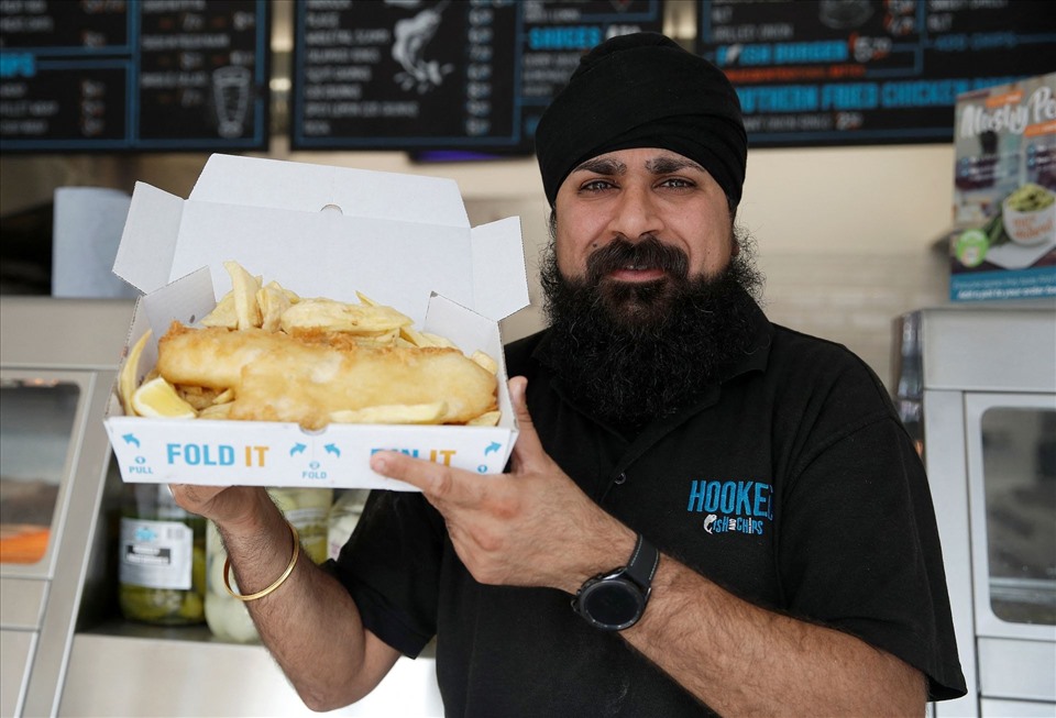 Bally Singh cầm một phần cá và khoai tây chiên bán tại cửa hàng Hooked Fish & Chips của anh ở London, Anh, ngày 25.5. Ảnh: Reuters