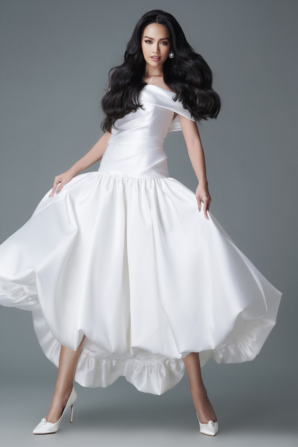 Nhà thiết kế Đỗ Mạnh Cường chú trọng vào việc tạo phom độc đáo cho trang phục. Chiếc váy trắng tạo điểm nhấn bởi những đường gấp nếp bất đối xứng. Phần thân váy được hạ dài xuống hơn thắt eo tạo điểm nhấn tôn vóc dáng của nàng hậu. Ảnh: Milor Trần