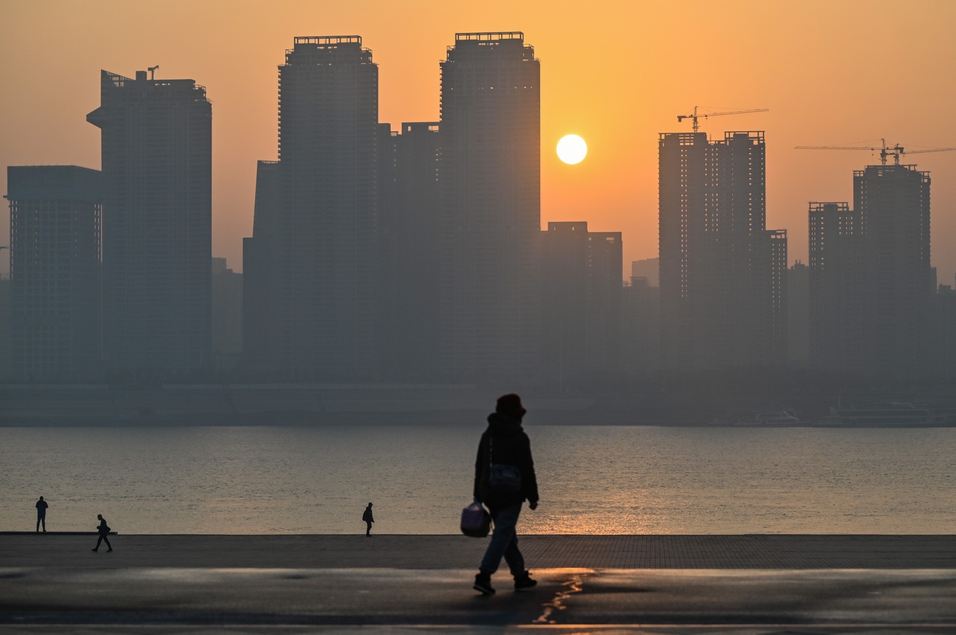 Mọi người đi bộ trong một công viên cạnh sông Dương Tử khi mặt trời mọc ở Vũ Hán, tỉnh Hồ Bắc, miền trung Trung Quốc vào ngày 21.1.2023. Ảnh: AFP