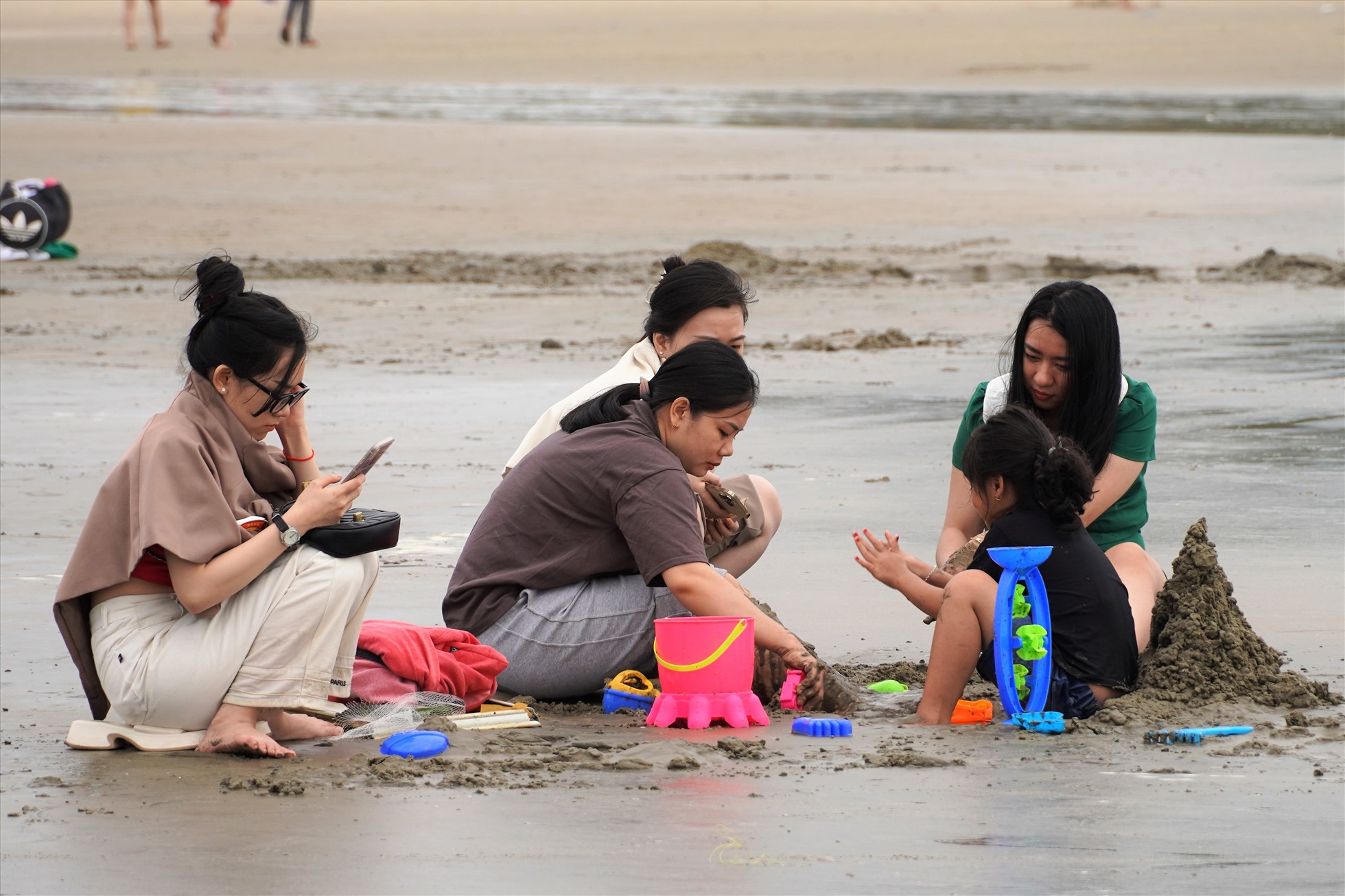 hoặc những nhóm gia đình cùng ngồi chơi cát trên bãi biển. Ảnh: Thành An