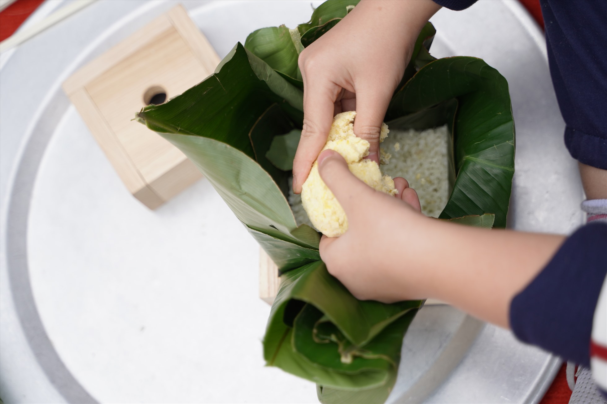 Các em học sinh được tự tay chuẩn bị lá, đổ gạo, đỗ, thịt và khéo léo gói thành chiếc bánh nhỏ xinh. Ảnh: Vân Trang