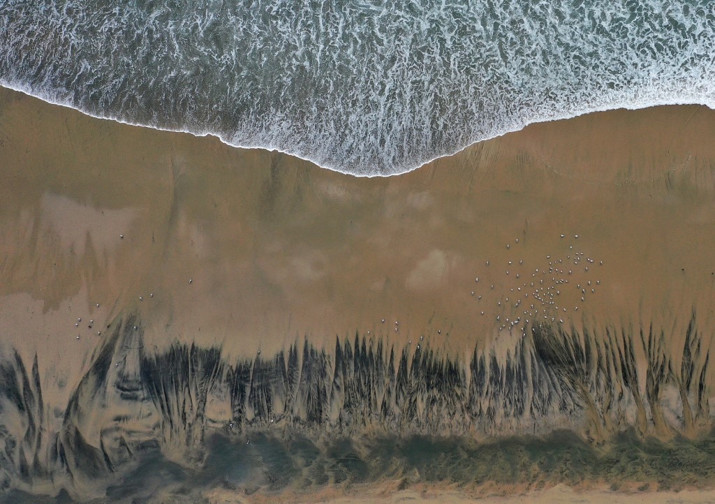 Dầu loang theo sóng dạt vào bờ biển. Ảnh: AFP
