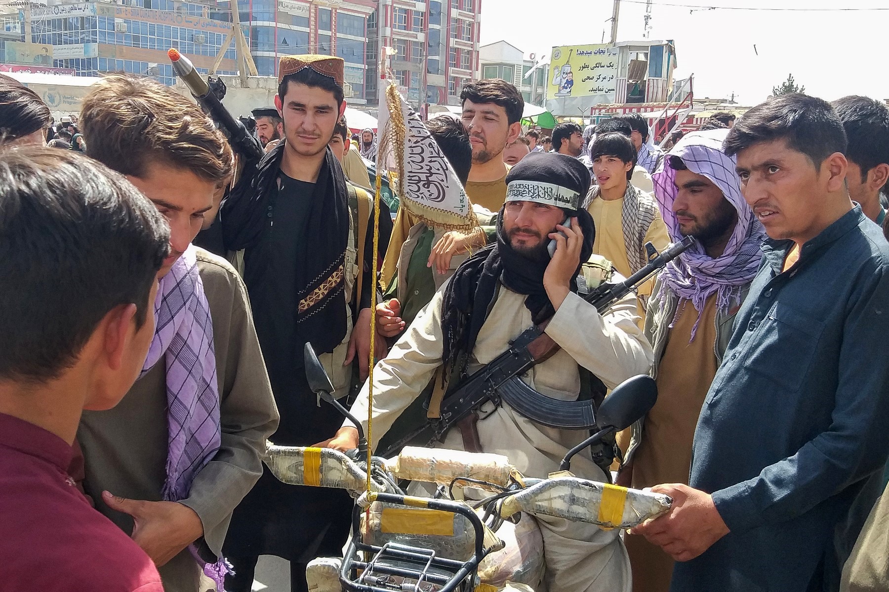 Người dân Afghanistan đứng quanh tay súng Taliban (giữa) tại Pul-e-Khumri vào ngày 11.8 sau khi Taliban chiếm được Pul-e-Khumri, thủ phủ tỉnh Baghlan, cách Kabul khoảng 200km về phía bắc. Ảnh: AFP