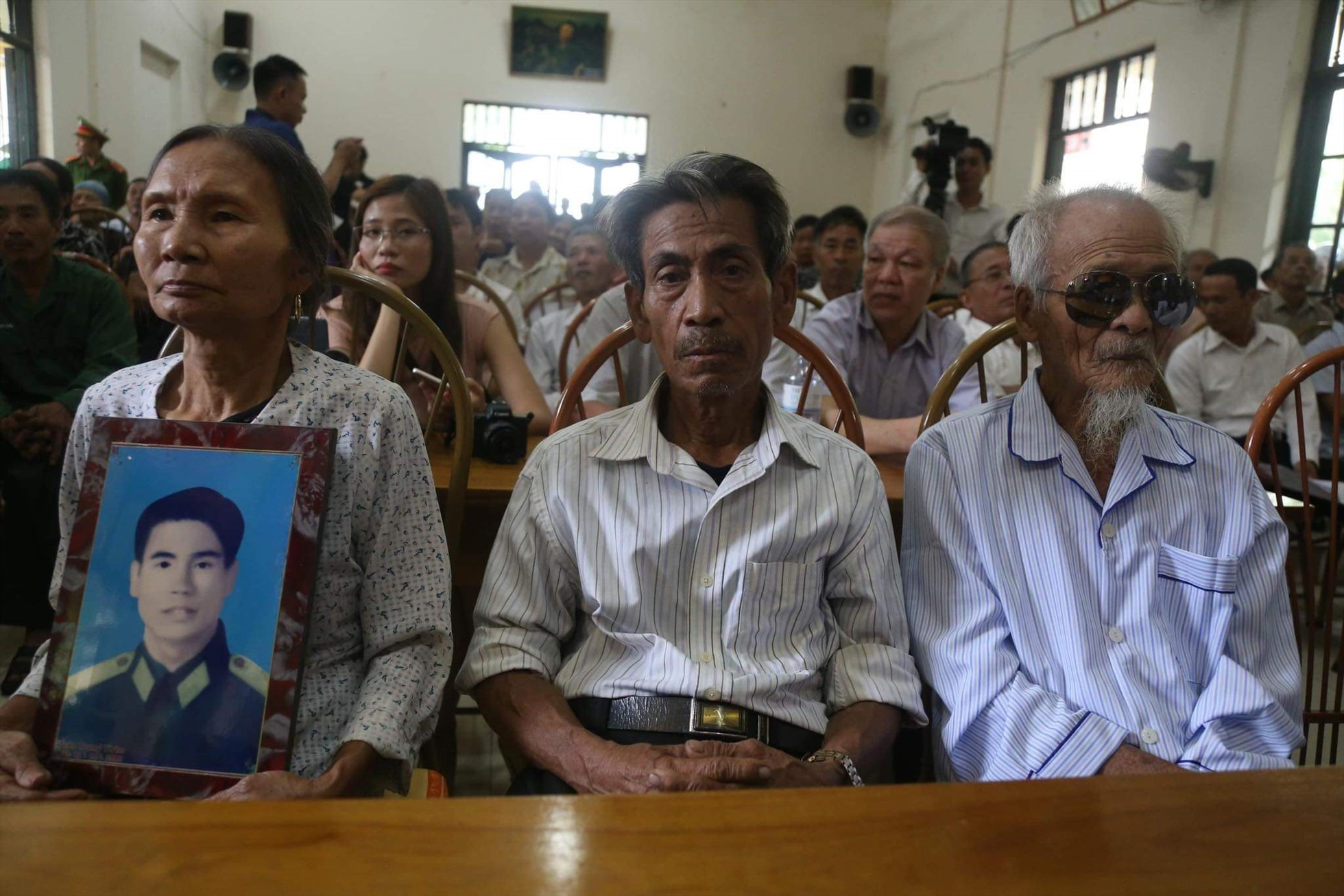 Vợ ông Trần Trung Thám ôm di ảnh của chồng ngồi cạnh ông Trần Ngọc Chinh (giữa) và ông Khổng Văn Đệ tại buổi cải chính công khai hồi tháng 10/2019. Ảnh: Người dân cung cấp