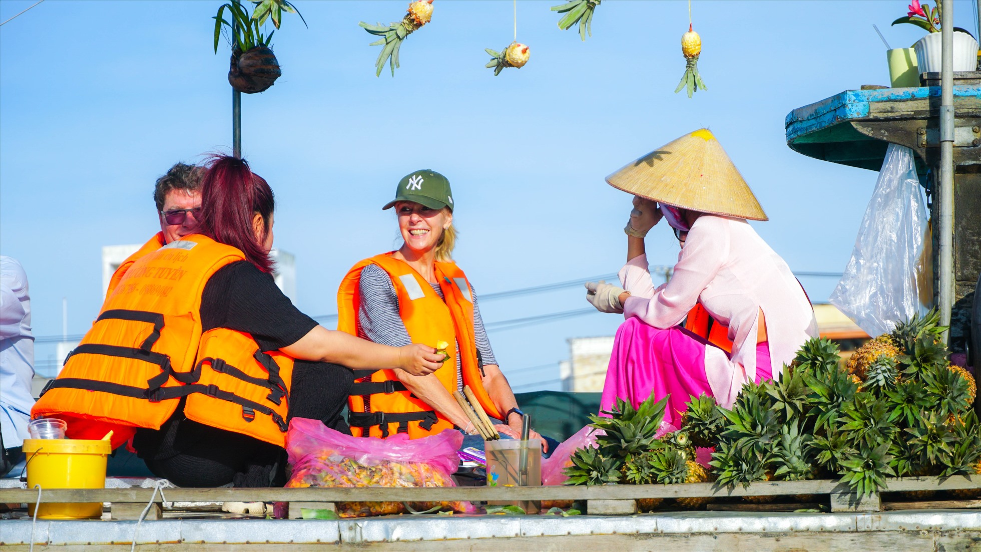Du khách nước ngoài trải nghiệm ăn dứa (khóm, thơm) trên ghe của thương hồ chợ nổi Cái Răng.