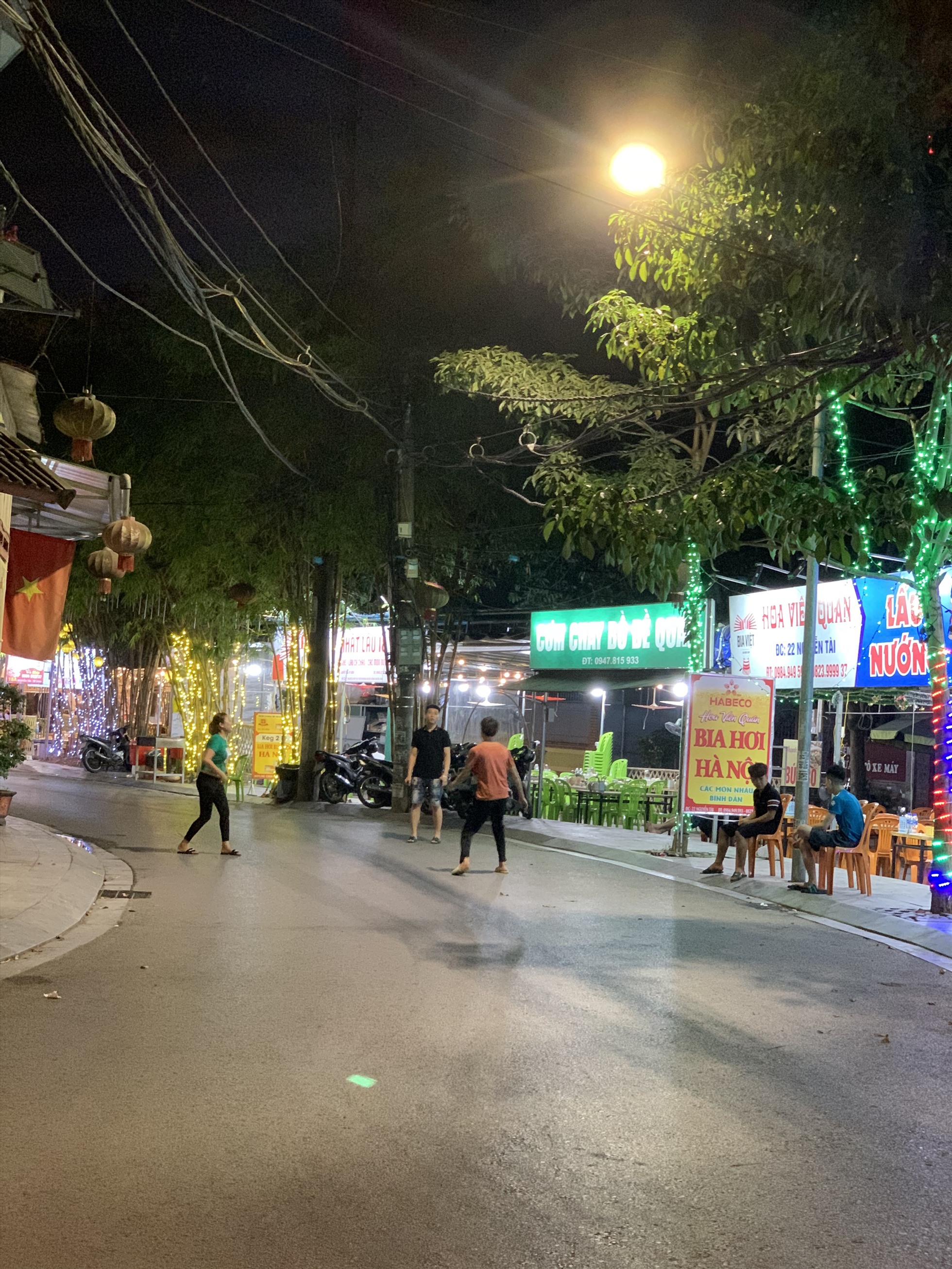 Nhiều nhân viên phục vụ tại một số quán ở cung đường Nguyễn Tài  ngồi không bấm điện thoại, rủ rau đá cầu ven vỉa hè,.. Ảnh: Quỳnh Trang