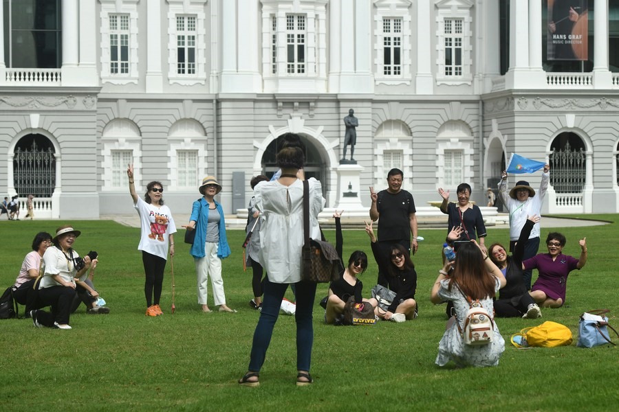 Du khách nước ngoài chụp hình bên ngoài Nhà hát kịch và Hòa nhạc Victoria ở Singapore. Ảnh: Xinhua