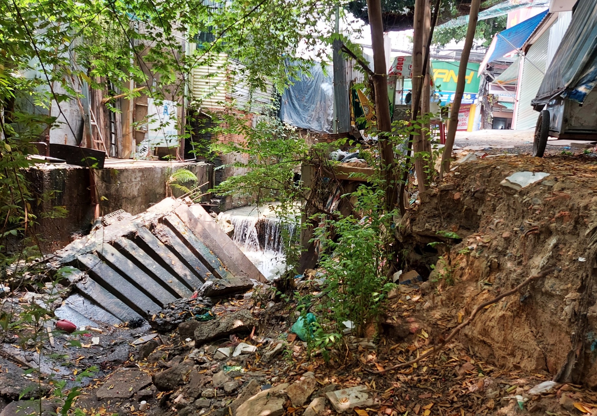 Sau trận mưa lớn vào năm 2021, nước chảy xiết làm một nhà dân bị sạt lở, phần cừ bê tông bị sạt ra suối gây sụp lún nặng nề.