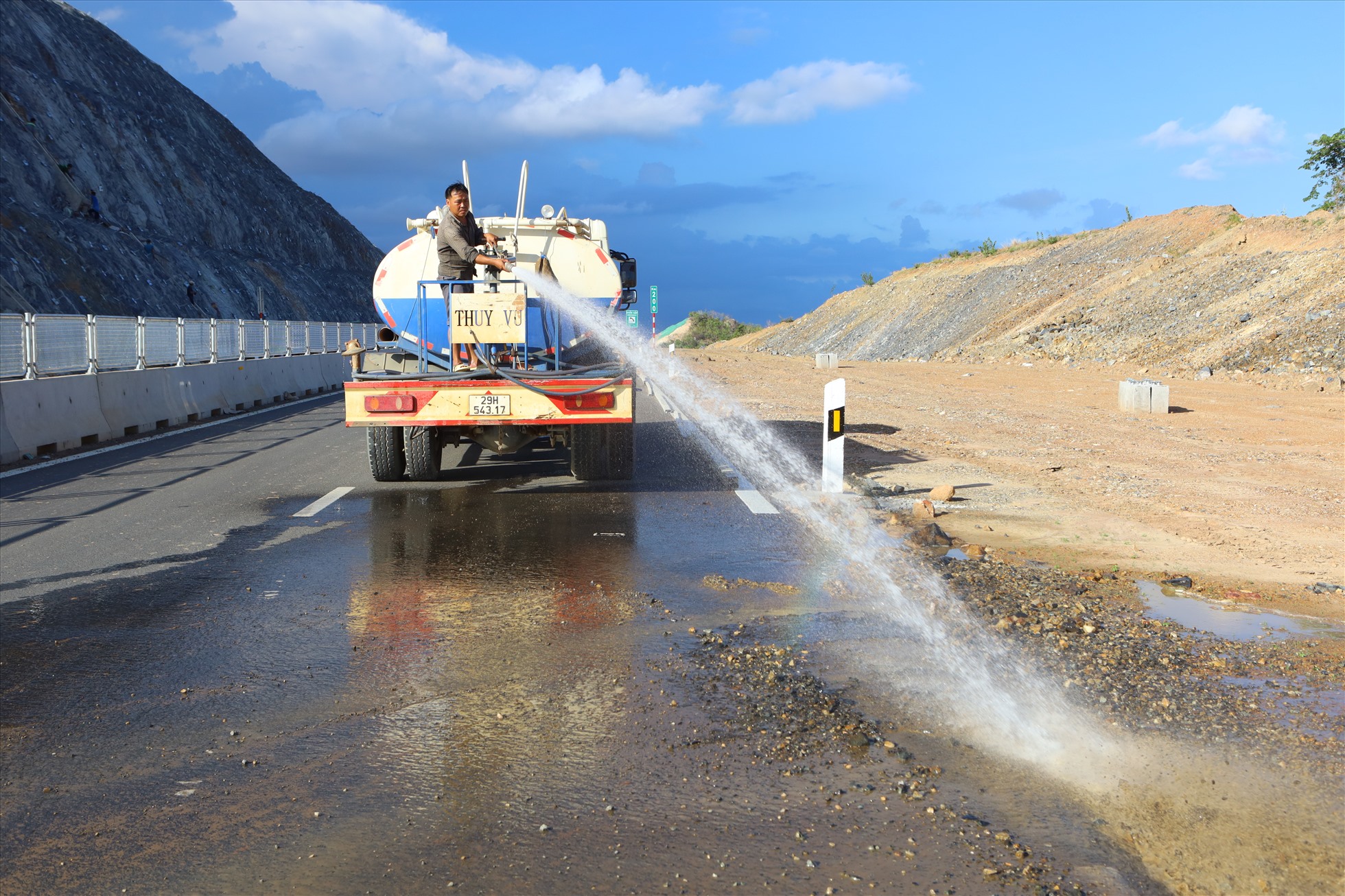 Xe rửa đường đang phun nước để vệ sinh mặt đường tại vị trí km200, đây là nơi xẻ núi để thi công đường cao tốc nên bụi đất bám nhiều dưới nền đường.