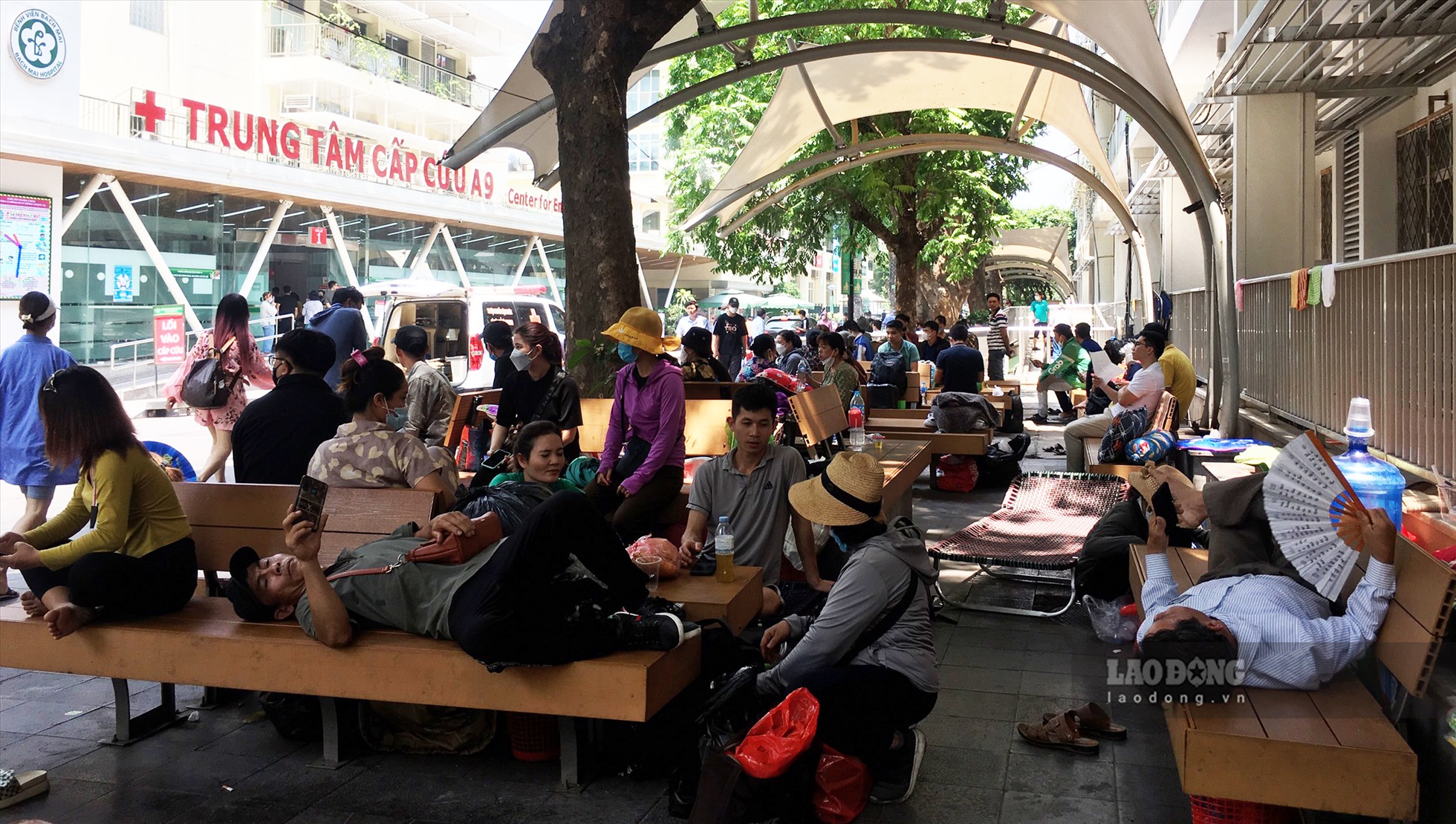 Theo ghi nhận vào khoảng 12h ngày 18.5, tại bệnh viện Bạch Mai, dưới thời tiết nắng nóng, nhiều người nhà bệnh nhân vẫn phải ngồi dưới gốc cây để tranh thủ ăn uống, nghỉ ngơi. Bất kể chỗ nào có bóng râm là có người ngồi tránh nắng.