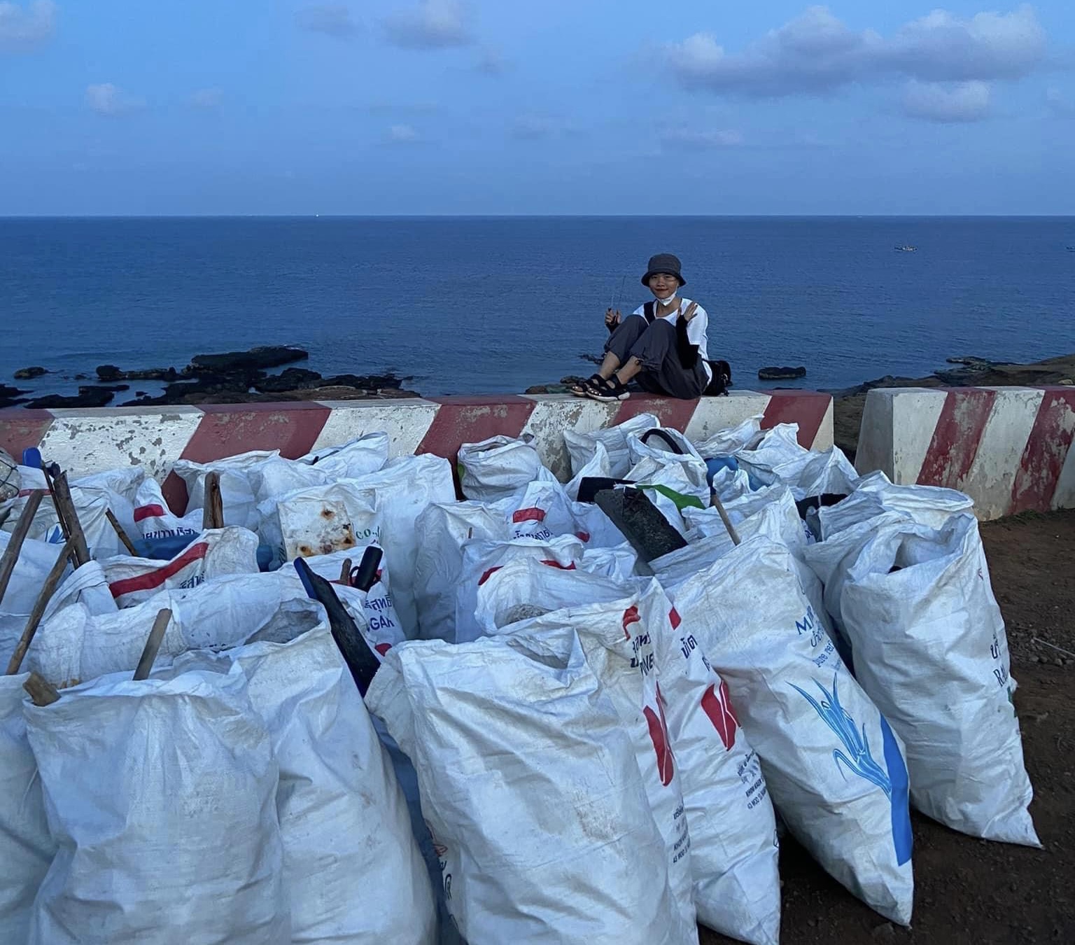 Tạ Thị Thuỳ bên các bao rác nhặt được và tập kết tại Dốc Phượt, đảo Phú Quý. Ảnh: NVCC