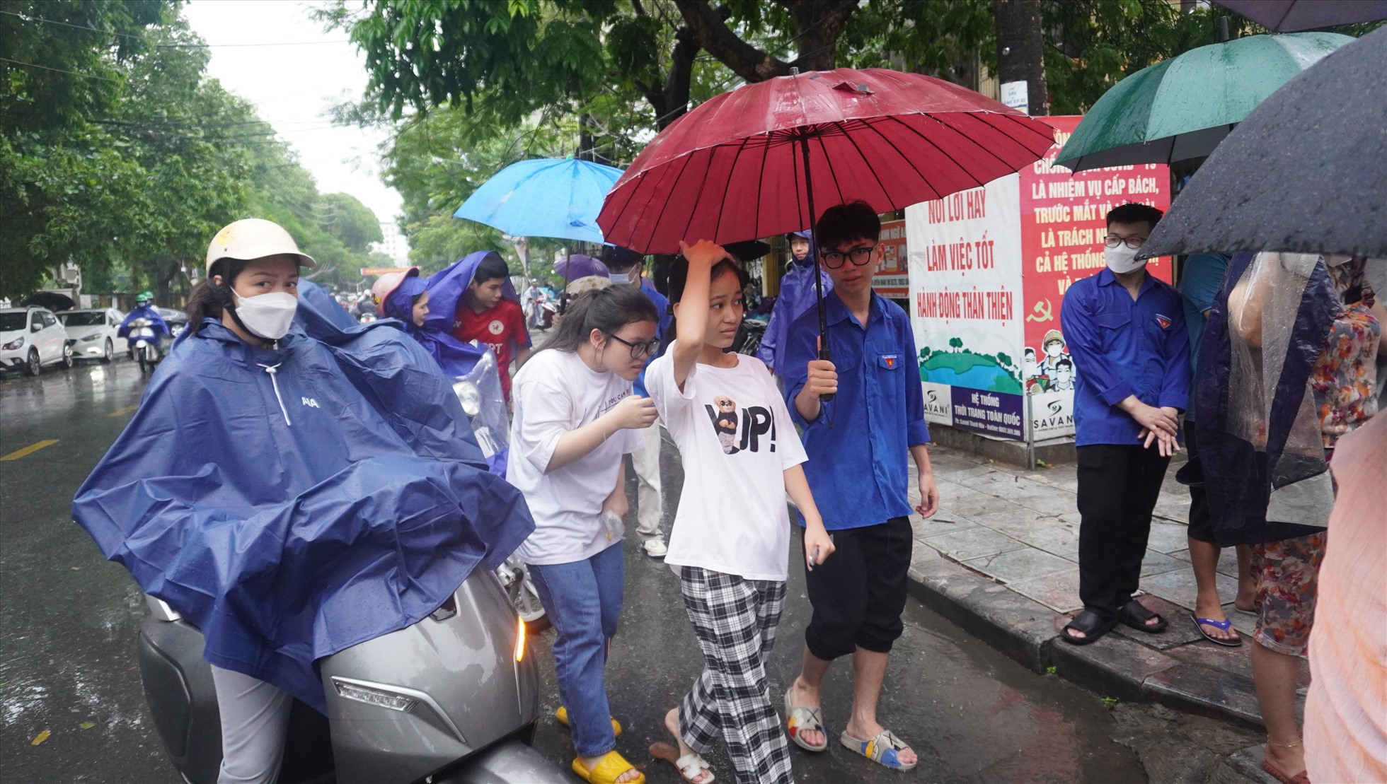 Do trời mưa, nên sau khi phụ huynh đưa con đến điểm thi Trường THPT Nguyễn Trãi, sẽ được các bạn sinh viên tình nguyện che ô đưa vào trong trường. Ảnh: Quách Du