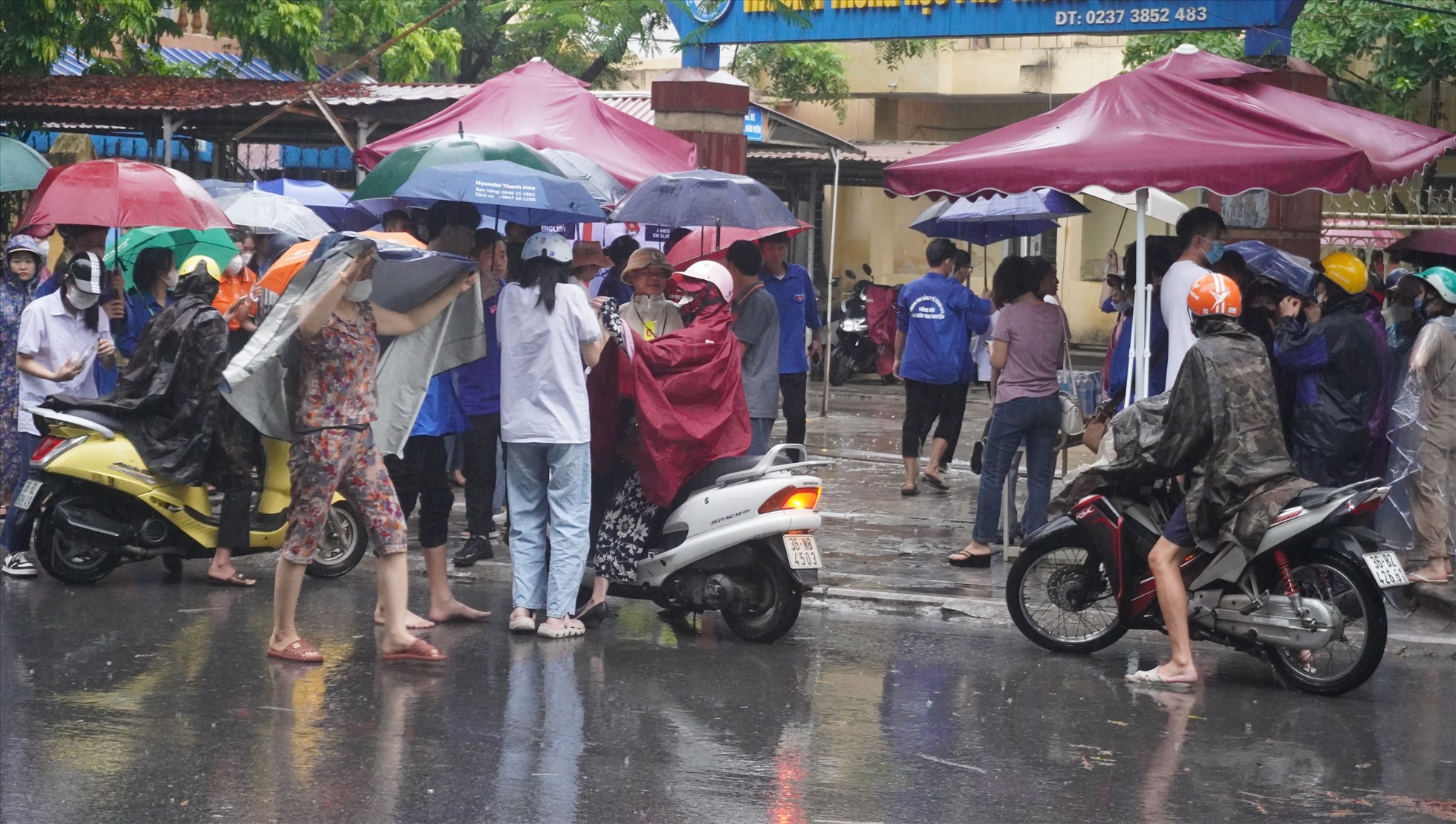 Do trời mưa, nên sau khi phụ huynh đưa con đến điểm thi Trường THPT Nguyễn Trãi, sẽ được các bạn sinh viên tình nguyện che ô đưa vào trong trường. Ảnh: Quách Du