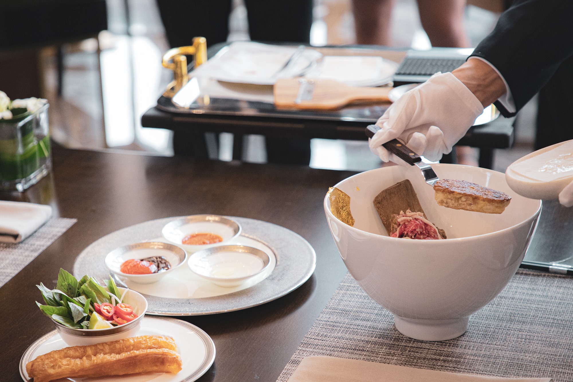 Khi phục vụ, nhân viên nhà hàng sẽ lần lượt đặt thịt bò, gan ngỗng, bào lát nấm truffle và dát vàng cho bát phở ngay trước mặt khách.