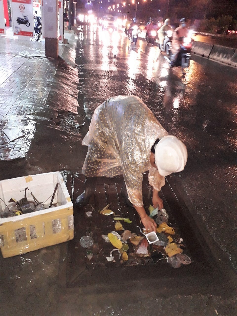 Công nhân Cty Quang Trung đội mưa đi vớt rác tại các miệng cống trên đường Nguyễn Hữu Cảnh vào chiều tối nay. Ảnh: Trường Sơn