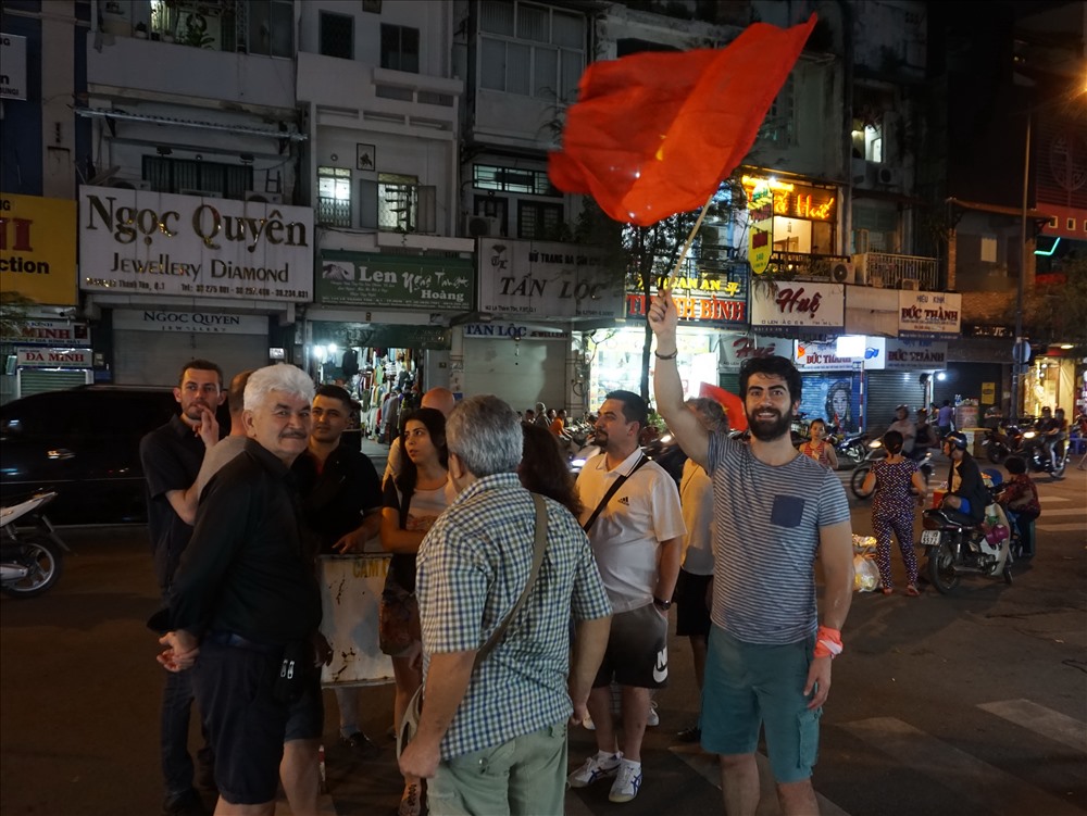Một nhóm người nước ngoài đứng gần chợ Bến Thành (quận 1, TPHCM) vẫy cờ và hò reo cùng Fan U23 Việt Nam.